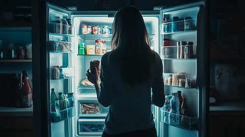 Woman standing in front of open refrigerator late at night, midnight snack