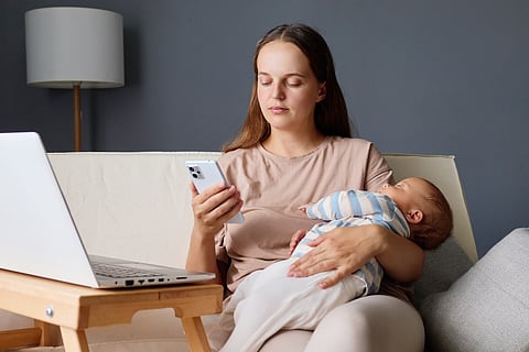 New mom holding baby while scrolling social media