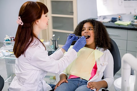 Pretty mixed raced teen girl in dentist chair, with mouth open, having dental examination.