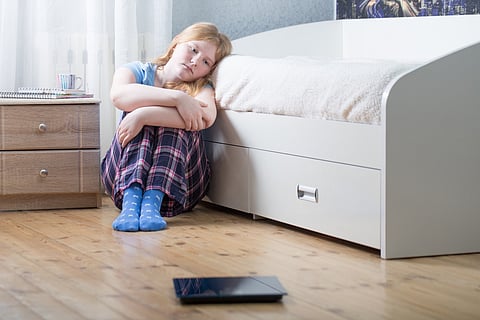 sad teenager girl with scales on floor