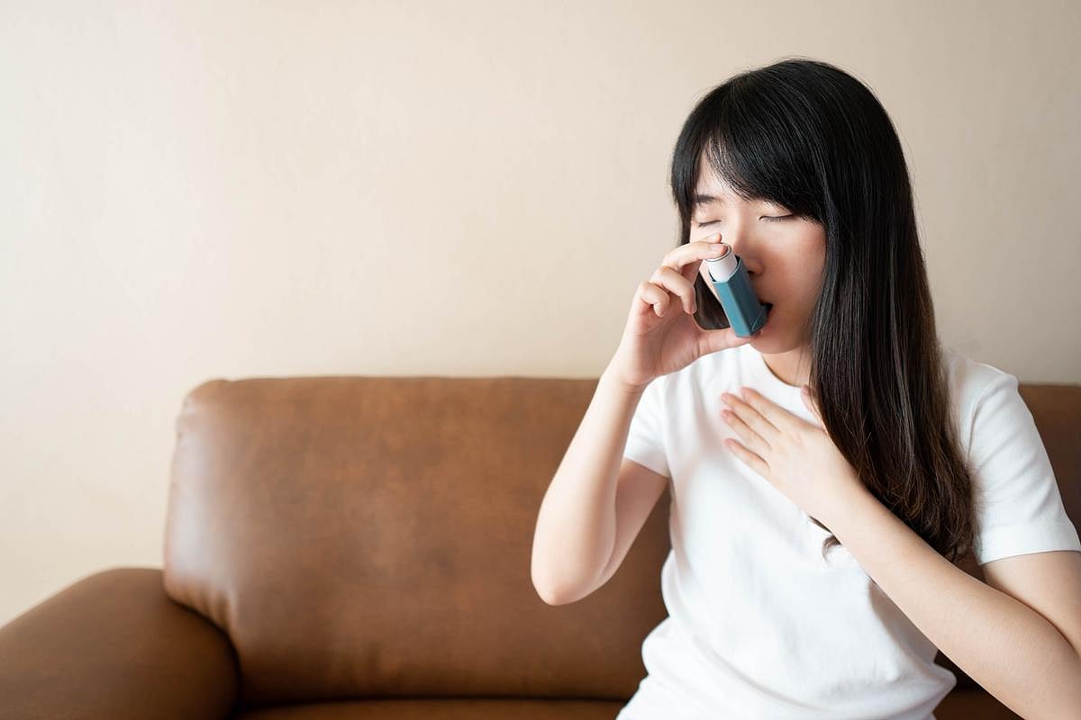 Mujer asiática joven utilizando un inhalador azul para el asma para aliviar un ataque asmático. Se utilizan productos