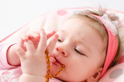 beautiful baby girl chewing amber teething necklace