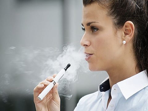 young female smoker smoking e-cigarette outdoors. Head and shoulders, side view