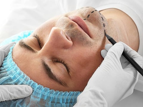 Plastic surgery concept. Hands in gloves marking male face