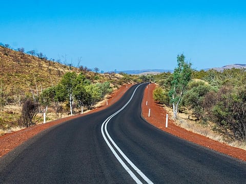 Road with dark tarmac leading between hills at Karijini National Park Australia