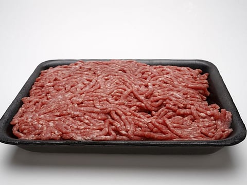 Raw ground beef in black styrofoam container on white background