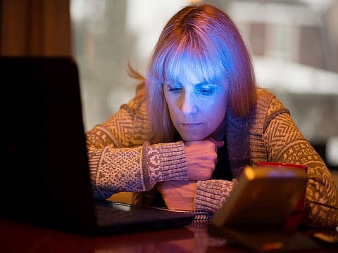 Middle-age woman with Seasonal affective disorder (SAD) working at home on computer with SAD LED light (lower right) which offers relief from seasonal depression.