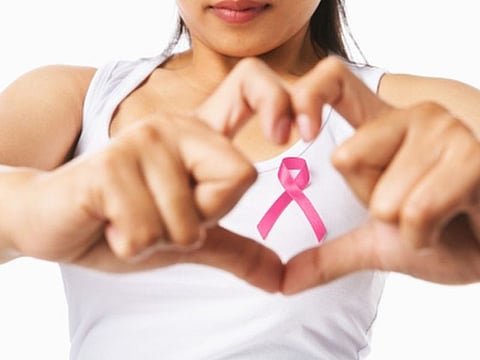 Heart framing from fingers on woman chest with pink badge to support breast cancer cause, PS: you can change the ribbon color to red to support AIDS cause as both using same symbol