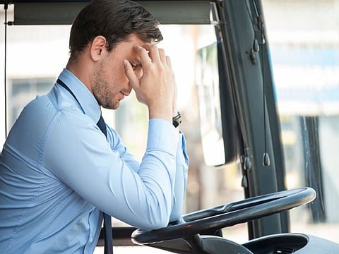 Handsome man is sitting at steering wheel of the bus. He is touching his head with frustration. The man has a terrible headache