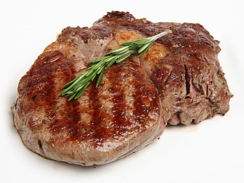 Close-up of a freshly griddled rib-eye steak resting on a white plate