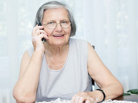 Senior woman sitting on the table and talking by phone.