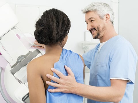 Mature male doctor assisting patient undergoing mammogram X-ray test in hospital