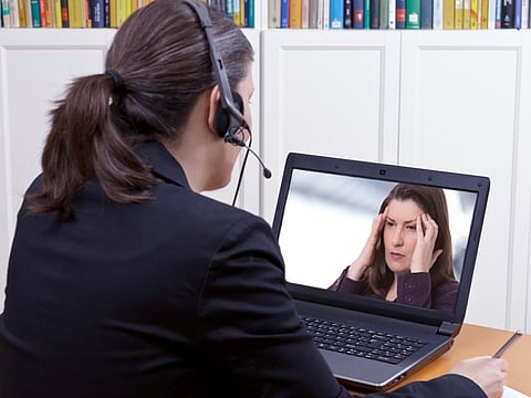 Woman with headset in front of her laptop writing something on a paper while making a live video call with a patient or client, copy space