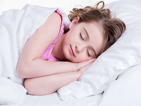 Adorable little girl in pink nightie sleeps in the bed on a white background.