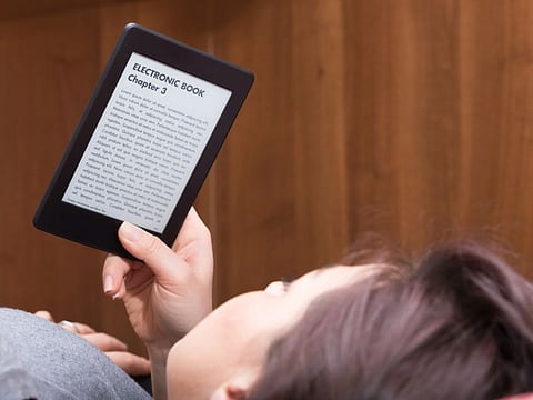 Brunette GIrl is focused reading an electronic bestseller with her Ebook Reader while she is on the bed. The text on the ebook reader is an "lorem ipsum"