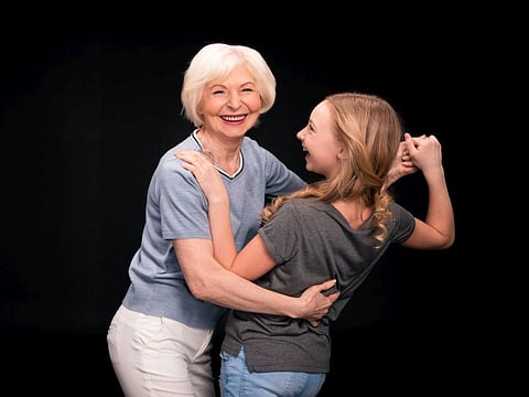 cheerful grandmother dancing with granddaughter isolated on black