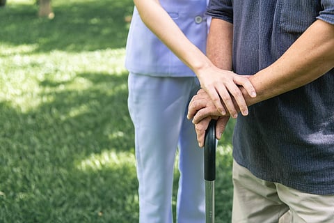 Comforting hand. Young nurse holding old man's hand in outdoor garden. Senior care, care taker and senior retirement home service concept. Close up shot.