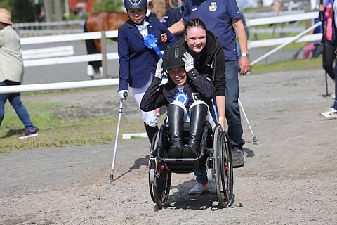 Jaana Kivimäki tuli ensimmäisenä palkintojenjakoon. Katri Aho avustaa pyörätuolin kanssa. Taustalla ruotsalainen hopeamitalisti.