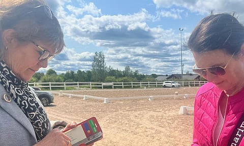 Koulutuomarit Irmeli Summanen ja Paula Nystén työssään kisapaikkana toimivan Hyyppärän kentän laidalla. Hirsitalli häämöttää taustalla. 