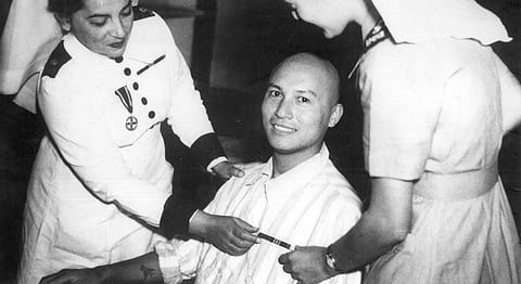 A black and white image of Ganju Lama displaying his Victoria Cross ribbon as two nurses stand by.