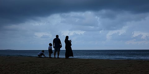 A silhouetted family of four stand on a beach in Sri Lanka, gazing at the ocean under a dark, stormy sky.