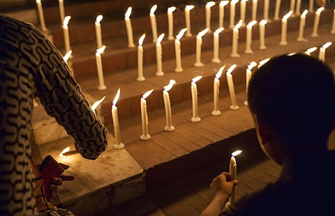 Two women are lighting candles during a vigil for the birangona in Bangladesh. Rows of white candles are placed on brick steps, their flames glowing warmly in the dark. 