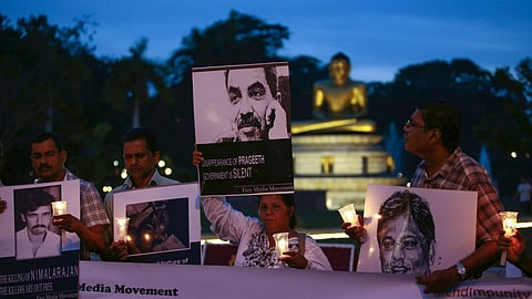 Wife of missing Sri Lankan cartoonist Prageeth Ekneligoda, Sandhya and media activists at a Black January vigil to commemorate abducted, tortured and killed Sri Lankan journalists. The vigil is at Viharamahadevi Park in Colombo, and it is evening. The Buddha statue at the park can be seen in the backdrop. Sandya holds a poster of her husband's face saying 'Disappearance of Prageeth, government is silent' in one hand, and a candle in the other.