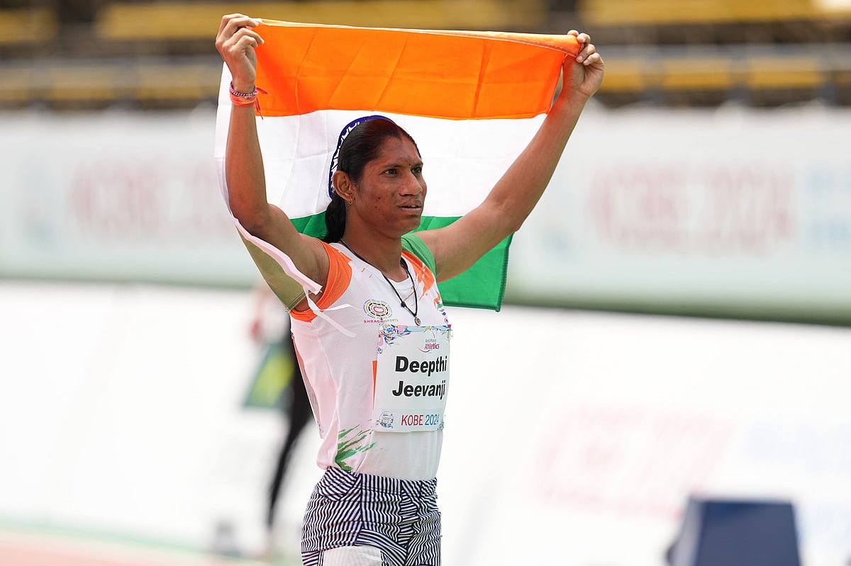 Deepthi Jeevanji, an Indian para-athlete with long black hair pulled back holds the Indian flag high with both her hands