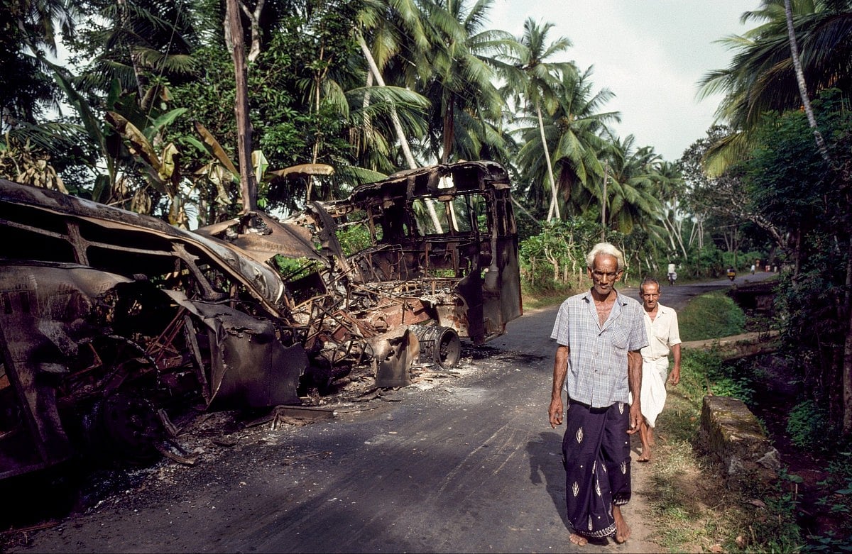 Civilians walk past a burnt-out bus in southern Sri Lanka in 1989, during the second JVP insurrection. 

