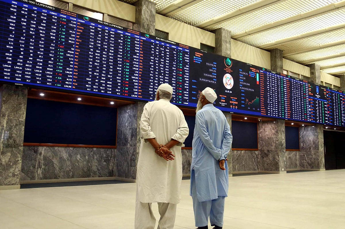 Two men dressed in salwar kurta with their hands behind their backs looking up at trading screens at the Pakistan stock excha
