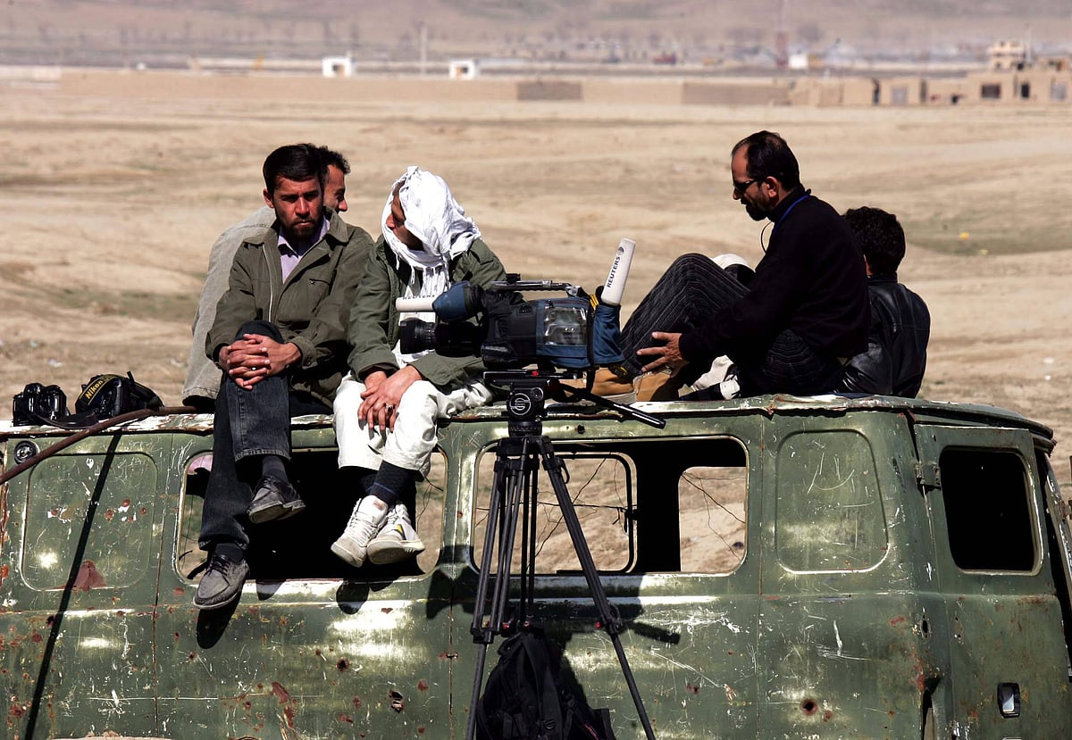 Five local journalists wait on the wreckage of a minibus while reporting on an uprising of Taliban prisoners in Pul-e-Charkhi