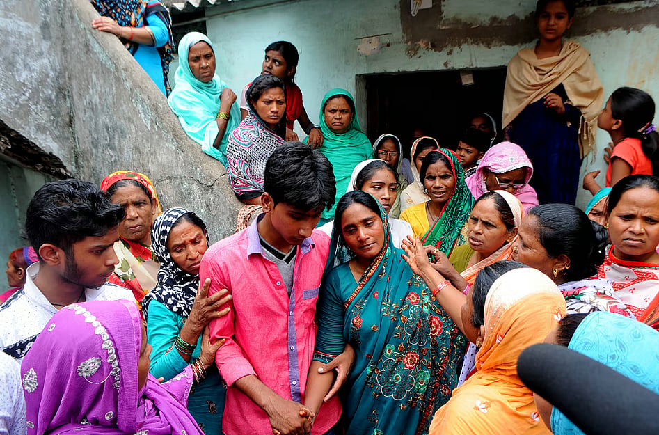 The widow (center) of a Muslim man murdered by a cow-protection group in Jharkhand in 2017.  She is wearing a green sari with red flowers, and her head covered. A man in a pink shirt is holding her hand. There is a crowd of women surrounding her. The rise of the Bharatiya Janata Party in India has come with a surge in violence against Muslim and Dalit communities by cow-protection vigilantes.