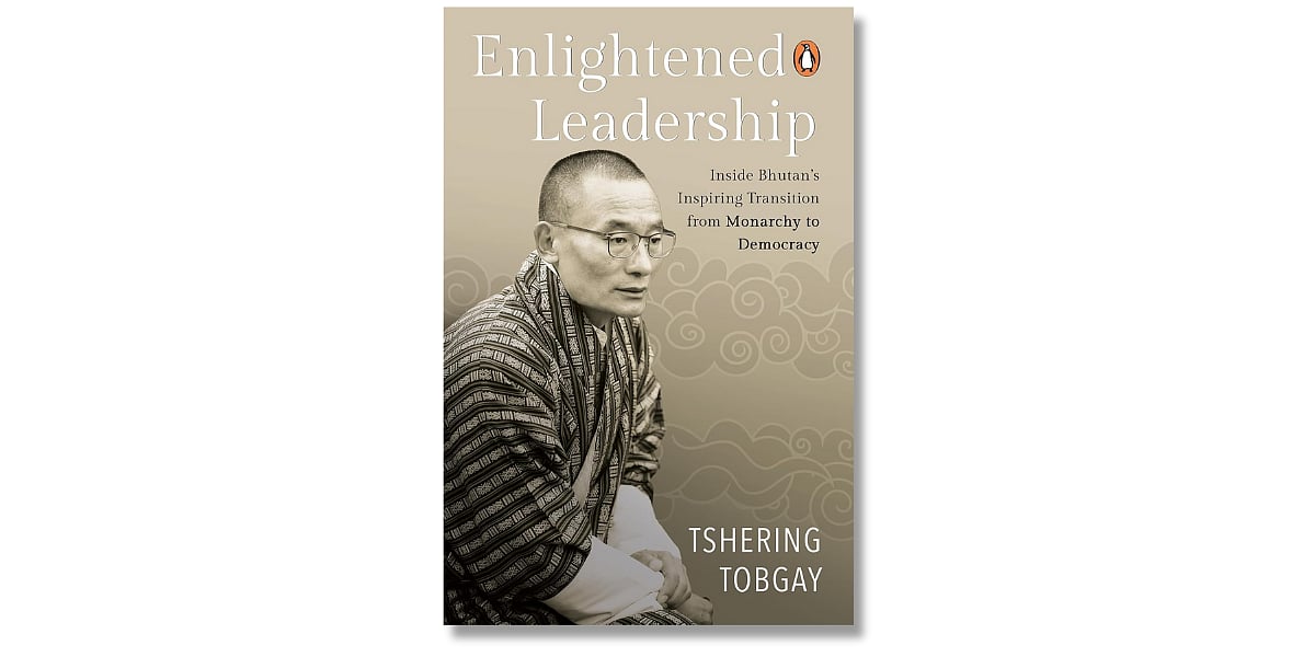Cover of the book 'Enlightened Leadership: Inside Bhutan’s Inspiring Transition from Monarchy to Democracy' by Tshering Tobgay. The background features stylised cloud patterns in soft beige tones. A sepia-toned photograph of Tshering Tobgay, wearing traditional Bhutanese attire and glasses, appears on the left side. The Penguin logo is visible near the top right corner near the title.