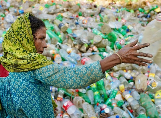 Photo of woman at a plastic recycling centre in Southasia. Her hair is covered with a yellow and green scarf and she wears a blue patterned kurta