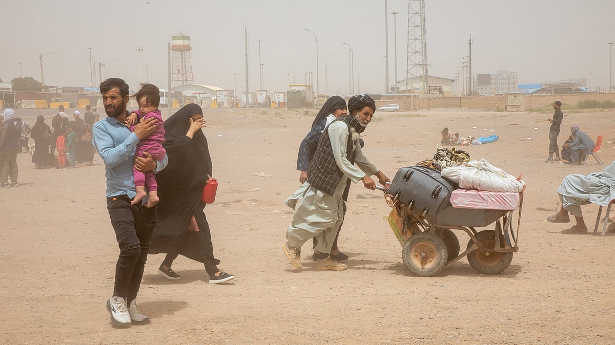 A man pushes a cart loaded with belongings and a family walks in a dust storm at the Islam Qala border crossing in Afghanista