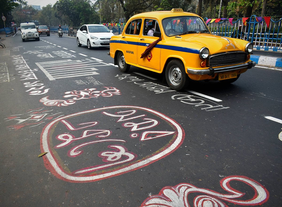 A yellow taxi drives along a street in Kolkata decorated with colourful Bengali messages painted on the asphalt for Internati