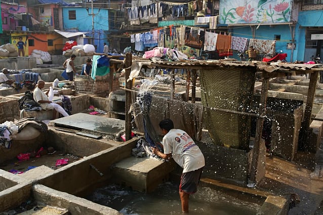 Photo of a man doing laundry in an open air laundry. More men can be seen in the background doing laundry