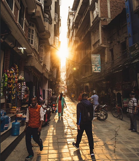Photo of a street with narrow alleyways at sunset, people are riding bikes and the streets are lined with shops