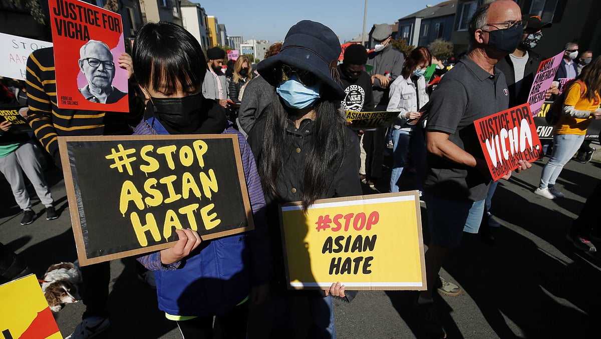 A crowd of people at a rally in San Francisco holding signs against anti-Asian hate. Two people in the foreground wear masks 