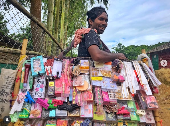 Photo of a man selling small items including hair accessories standing near a chain link fence. 