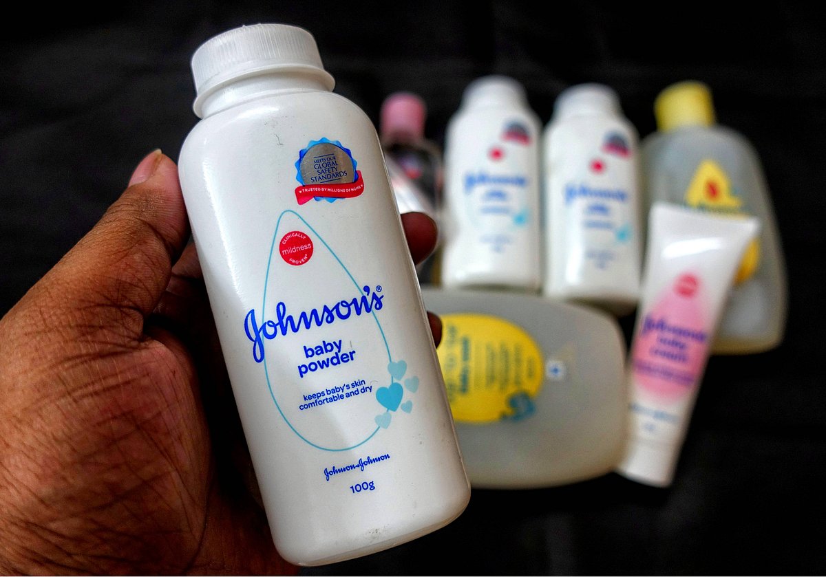 A hand holds a bottle of Johnson’s baby powder in the foreground, with several other Johnson’s baby care products blurred in 