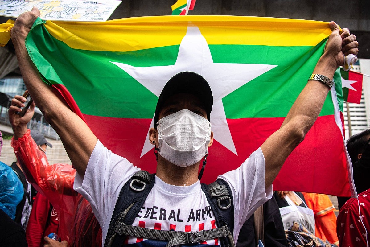 A protester wearing a face mask and cap holds up the flag of Myanmar during a Spring Revolution demonstration in Bangkok. The
