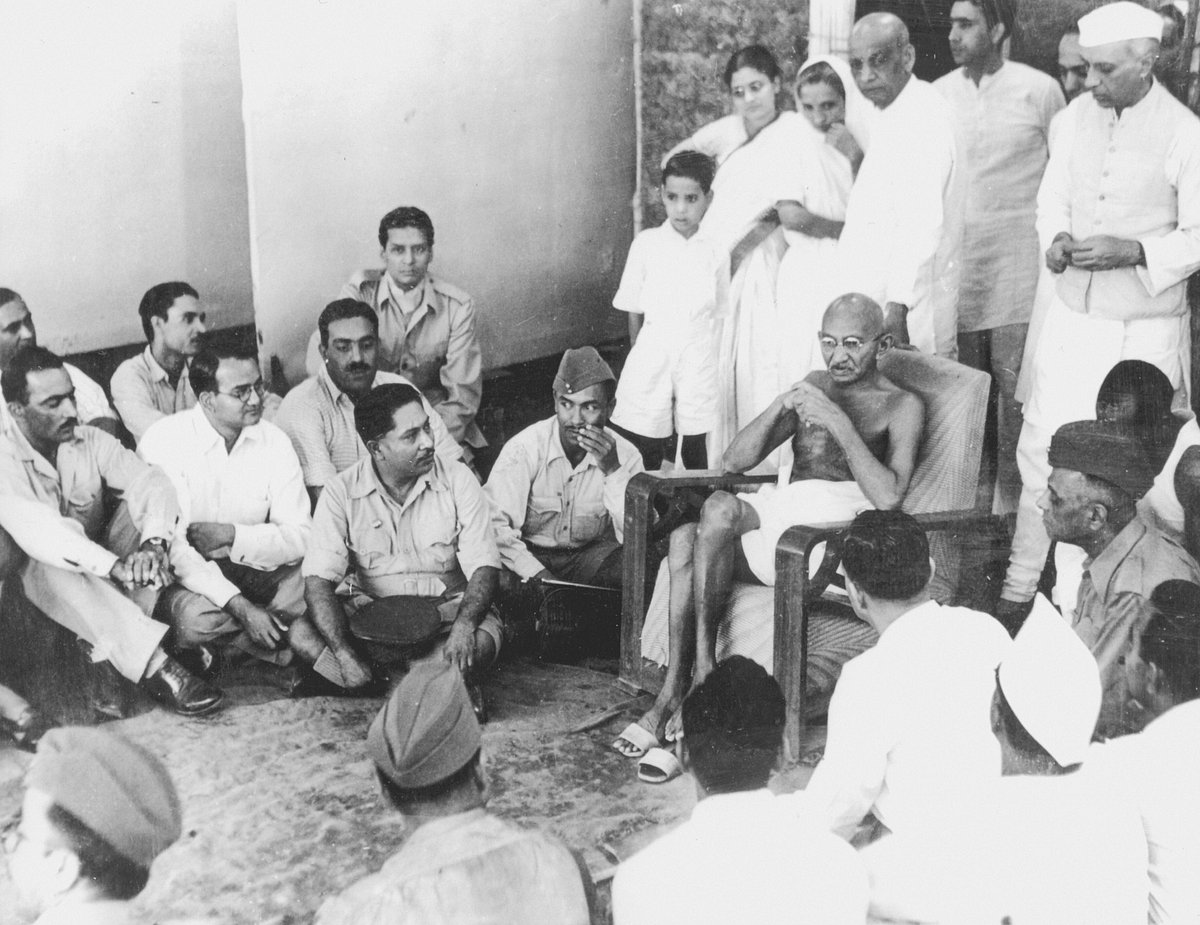 Mohandas Gandhi sits on a chair during a visit to a bhangi colony. He is surrounded by army officers in uniform. Jawaharlal N