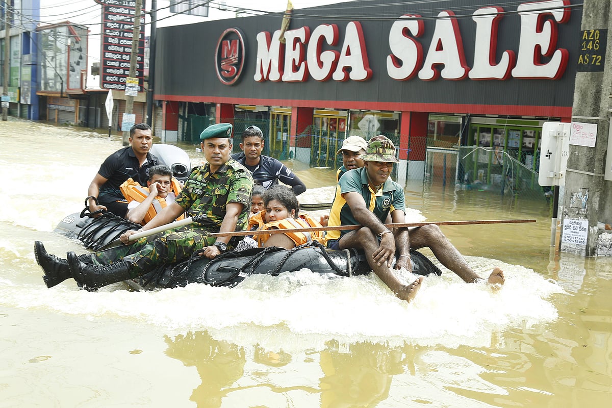 Photo shows a rubber dinghy moving through high floodwater. A man in Sri Lanka Army uniform is in front, along with a volunte
