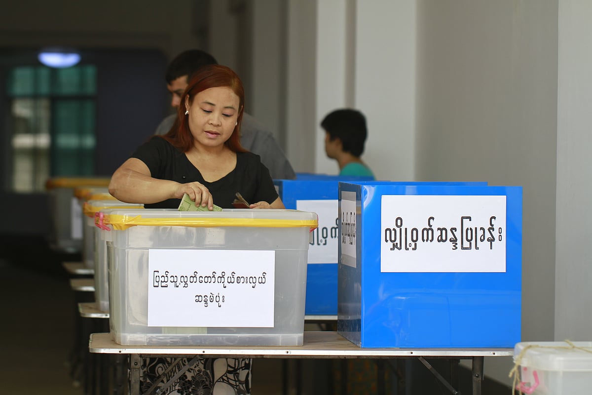 Woman casting a ballot in a box. A man can be seen behind her also casting a vote. The ballot box has writing on it in Burmes