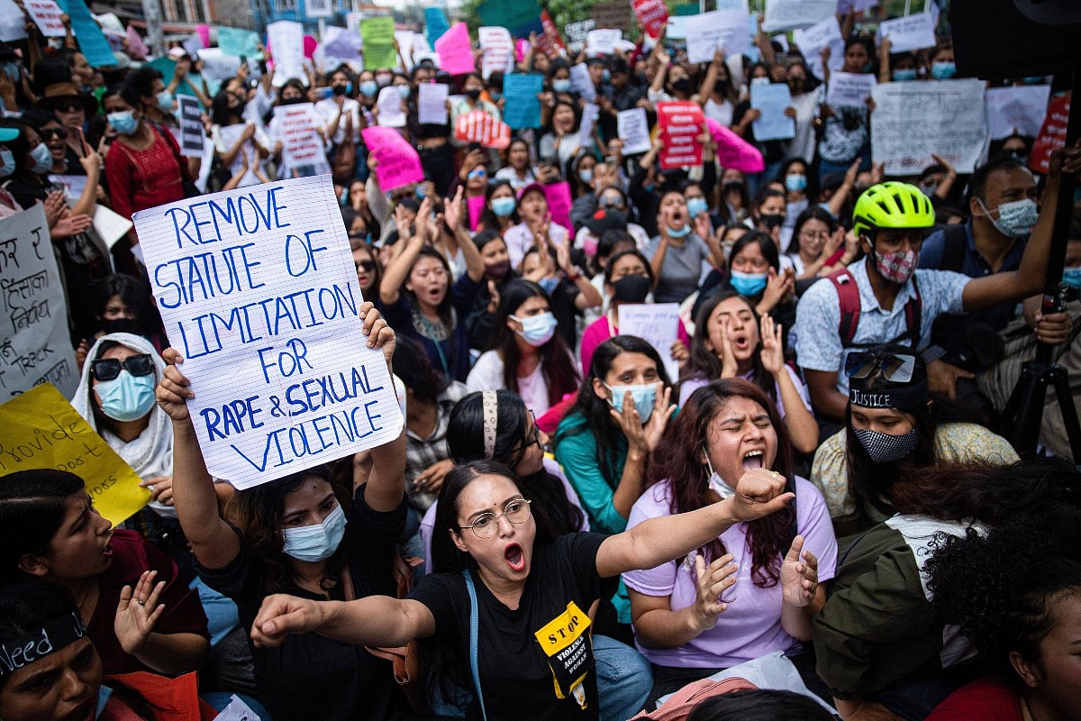 A large crowd of protesters in Kathmandu chant and raise fists while holding signs during a demonstration. In the foreground,
