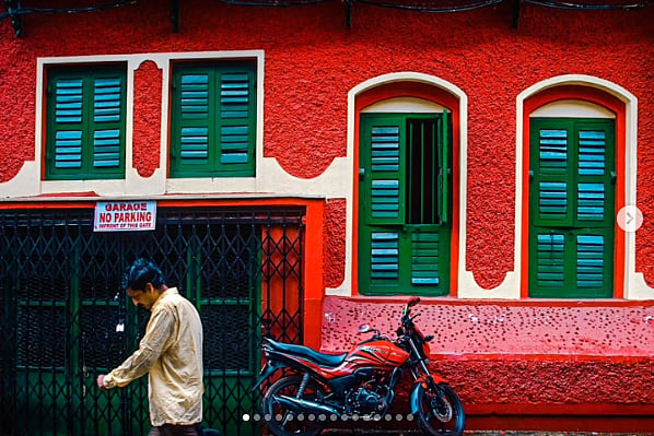 Photo of a man walking past a bright red wall. There are dark green windows set into the wall with blue shutters. A sign says 'Garage. No Parking'. 