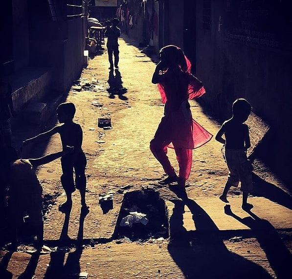 Girl playing in a shanty in low light. Three other children play around her. 