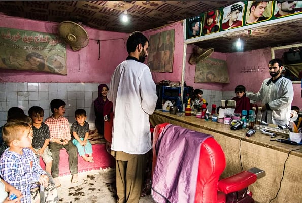 Man in a barbershop with pink walls. The clients are all children waiting to cut their hair. 