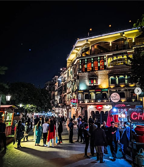 Photo of a street at night, lit up with many restaurants. People can be seen walking through the crowded street. 